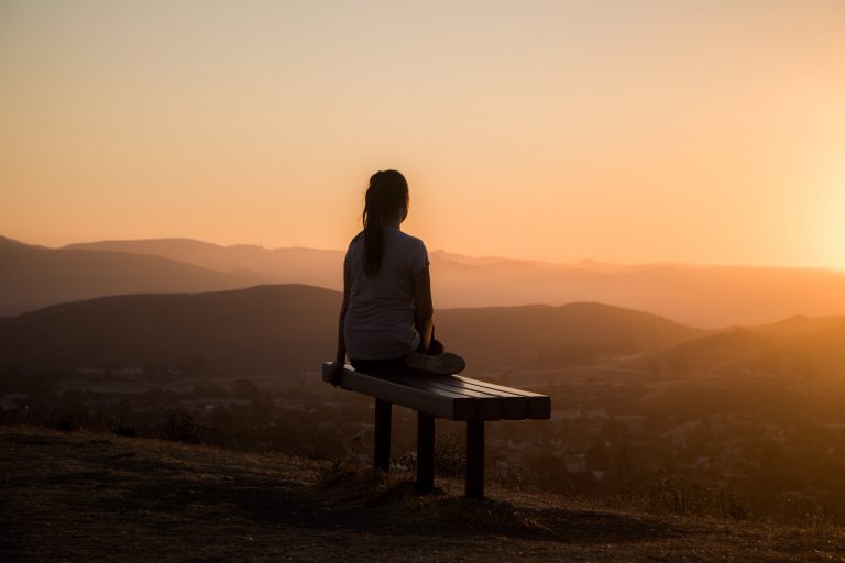Frau sitzt bei Sonnenuntergang in der Natur und wendet Techniken des Autogenen Trainings an